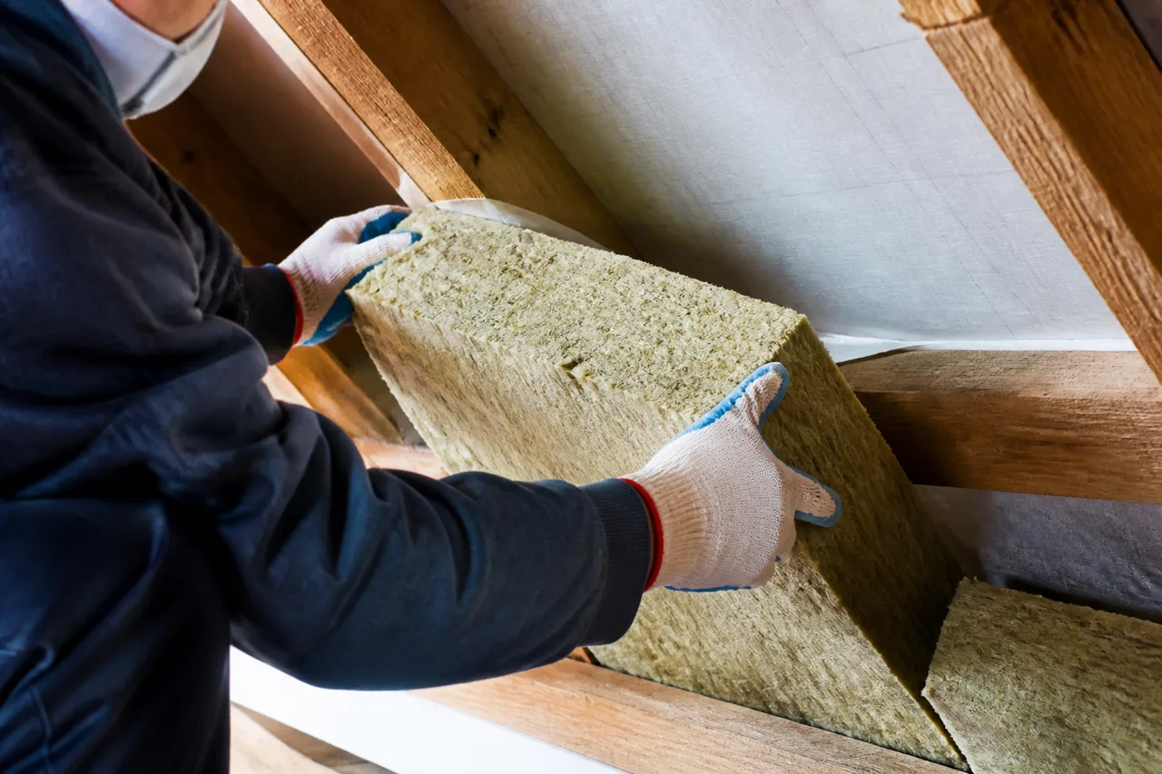 Trabajador colocando un panel de lana mineral entre vigas de madera del techo