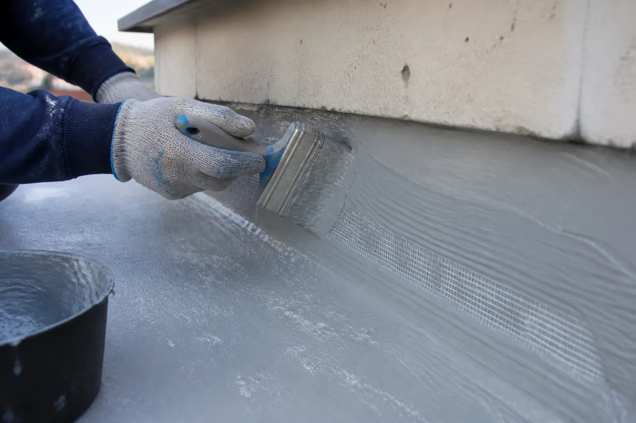 Trabajador aplicando impermeabilizante con pincel y malla en un parapeto de losa